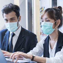 Two people wearing face masks having a discussion in front of laptop